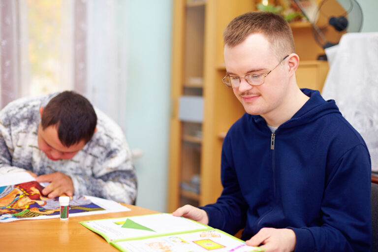 Young adult with disabilities reads at a table in a center.